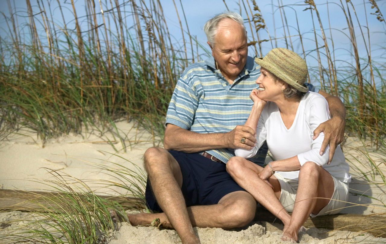 Elderly couple sitting and embracing on a sand dune at the beach