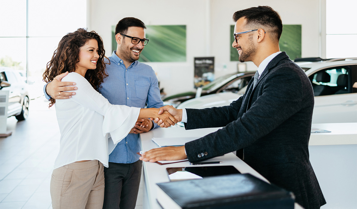 Man and woman shaking a car salesman's hands at an auto dealership