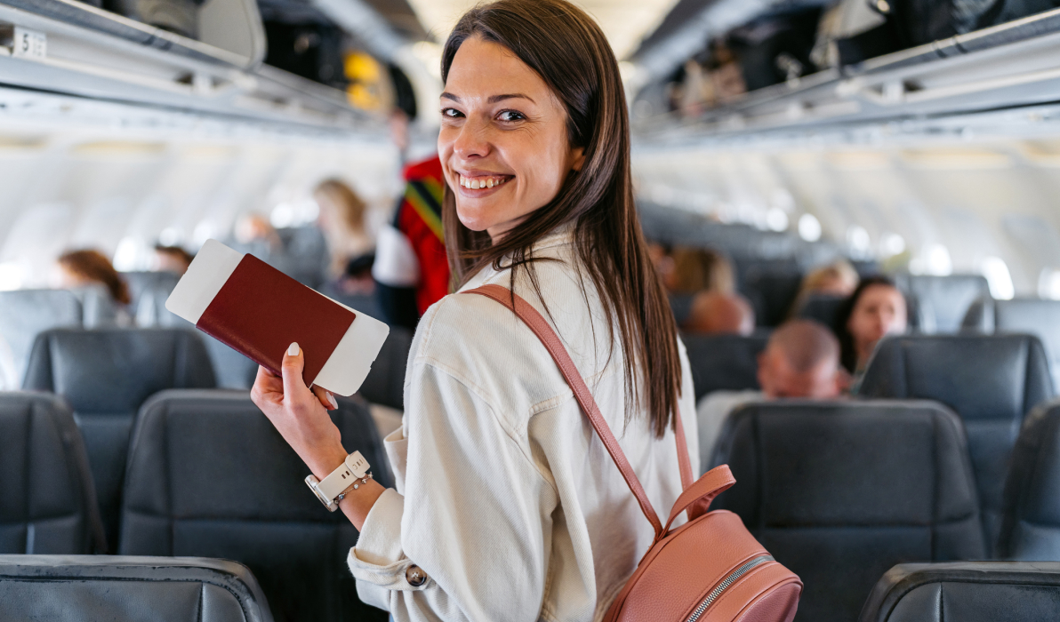 Young woman holding her passport and boarding pass while finding her seat on an airplane