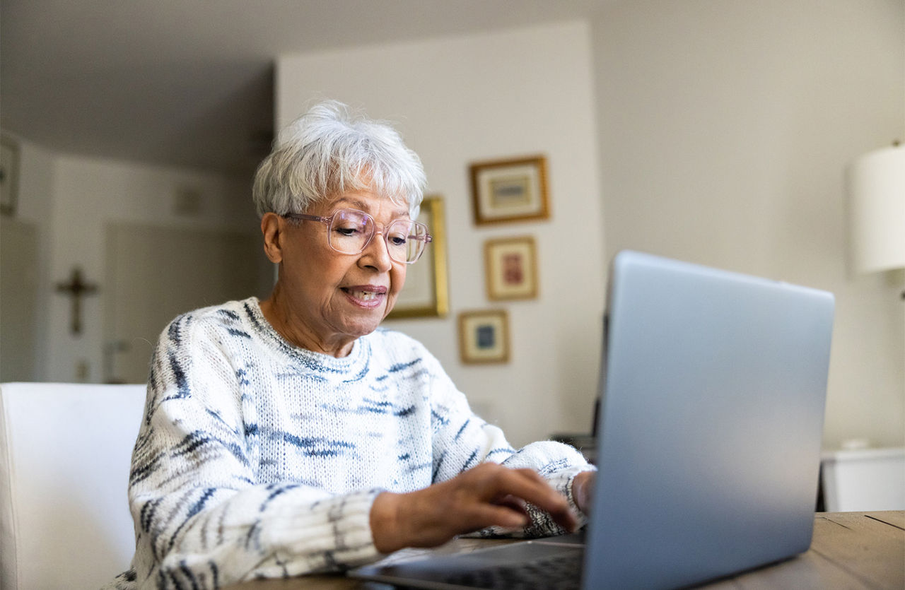 An elderly lady sitting at her kitchen table using her laptop